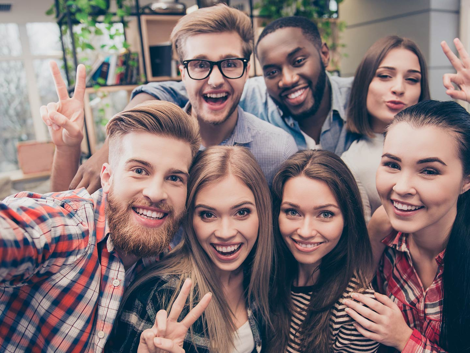Sieben junge Erwachsene lächeln in die Kamera und zeigen positive Handzeichen